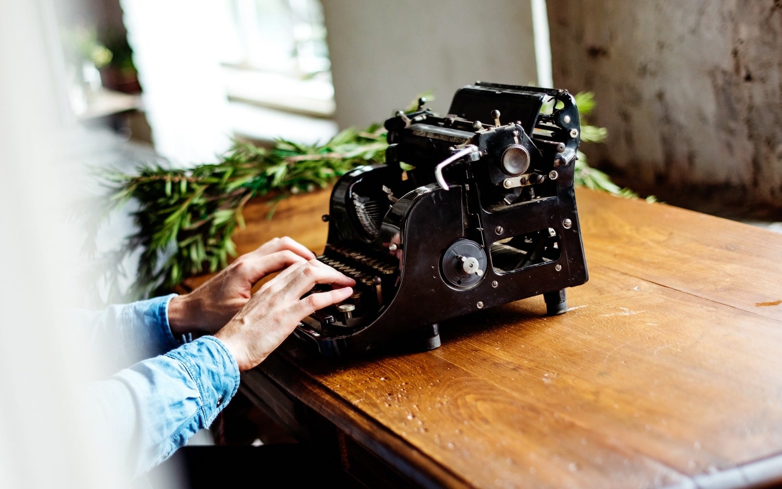 Hands type on a vintage typewriter beside a window