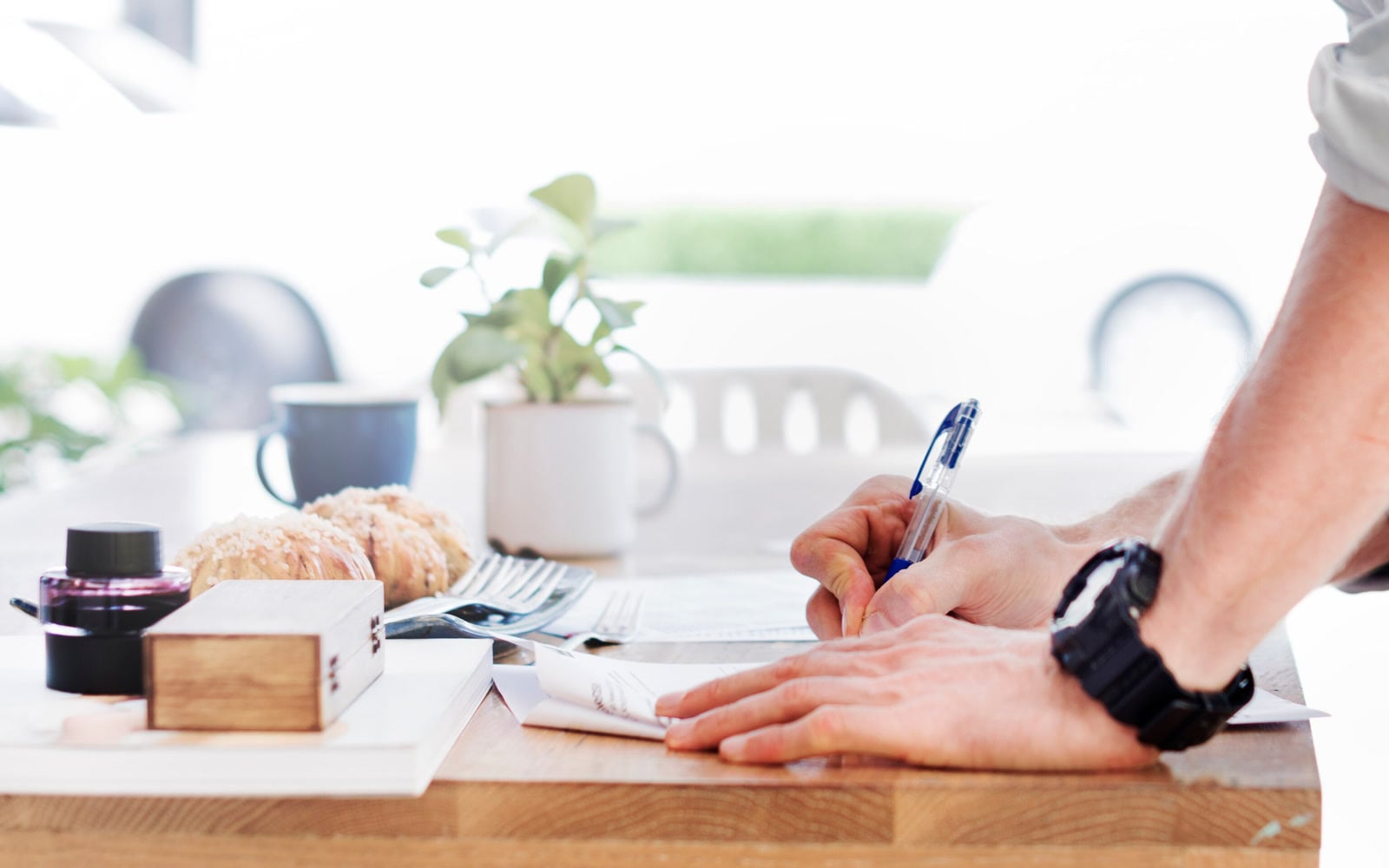 A person writes notes at a bright desk