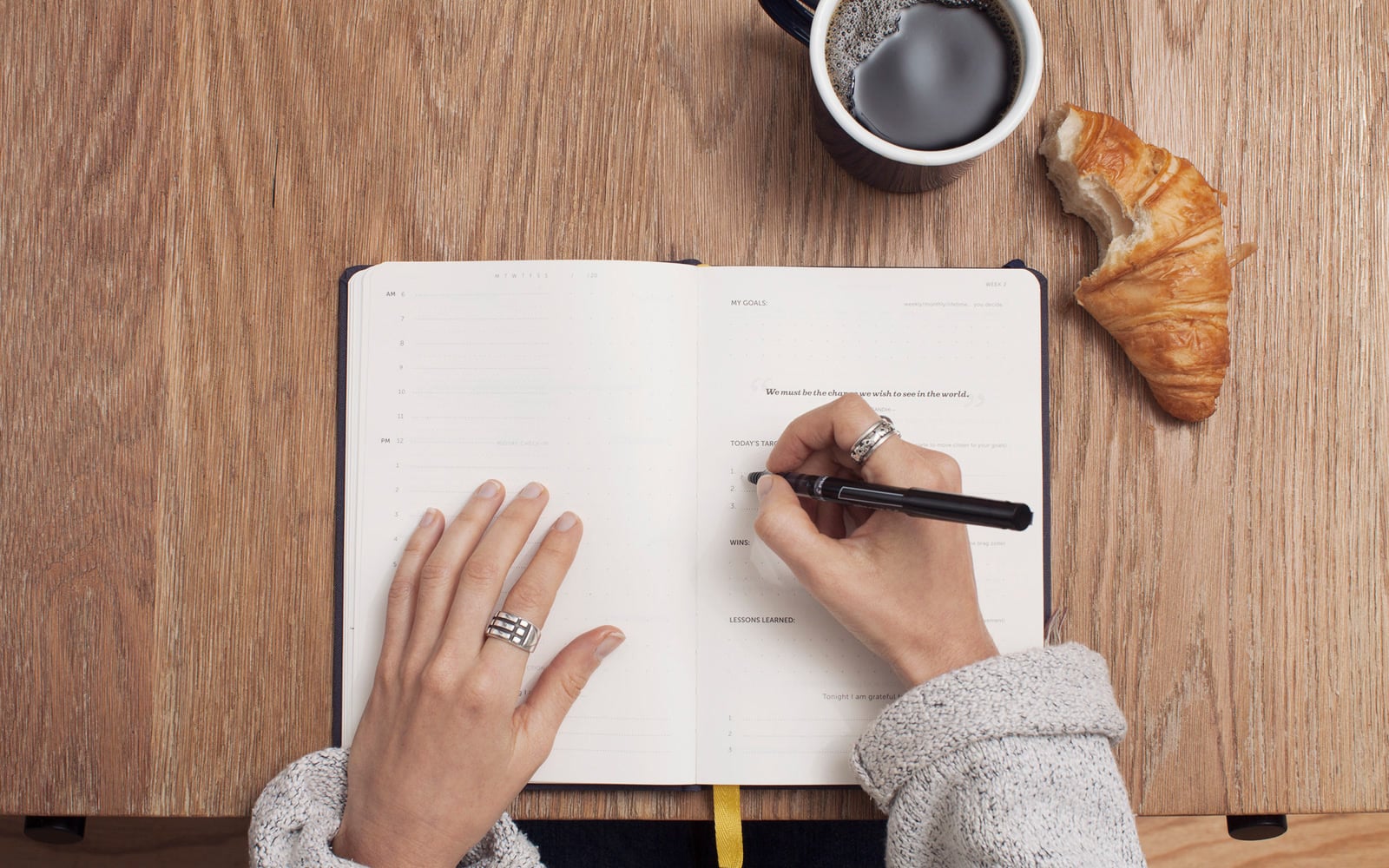 A person writes in a journal beside a cup of coffee