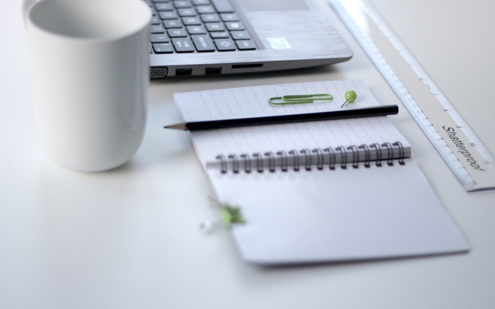 A ruler, notebook, pencil, and laptop on a white desk